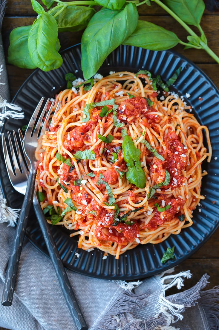 spaghetti on a black plate with fresh basil