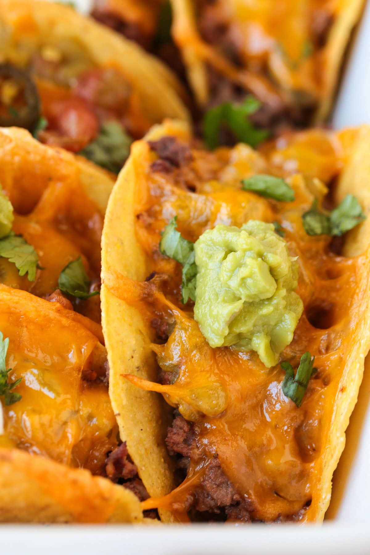 Kick up taco night with these addicting, crispy Baked Tacos! Super easy to make for parties or every day dinners, and everyone loves them! taco in baking dish with dollop of guacamole