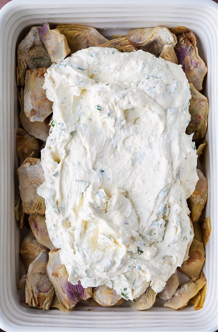 cream cheese sauce on top of artichoke hearts in casserole dish