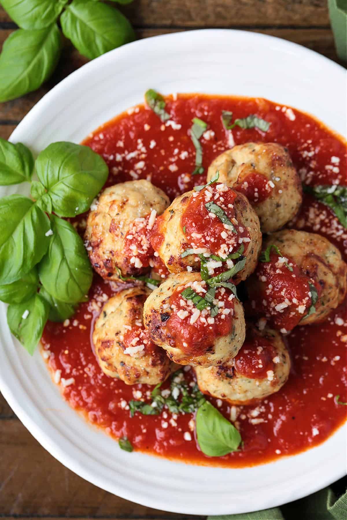 Our Air Fryer Turkey Meatballs are super flavorful and juicy! An easy to make dinner recipe that's ready to serve in just 15 minutes! turkey meatballs stacked on a dinner plate with sauce and basil