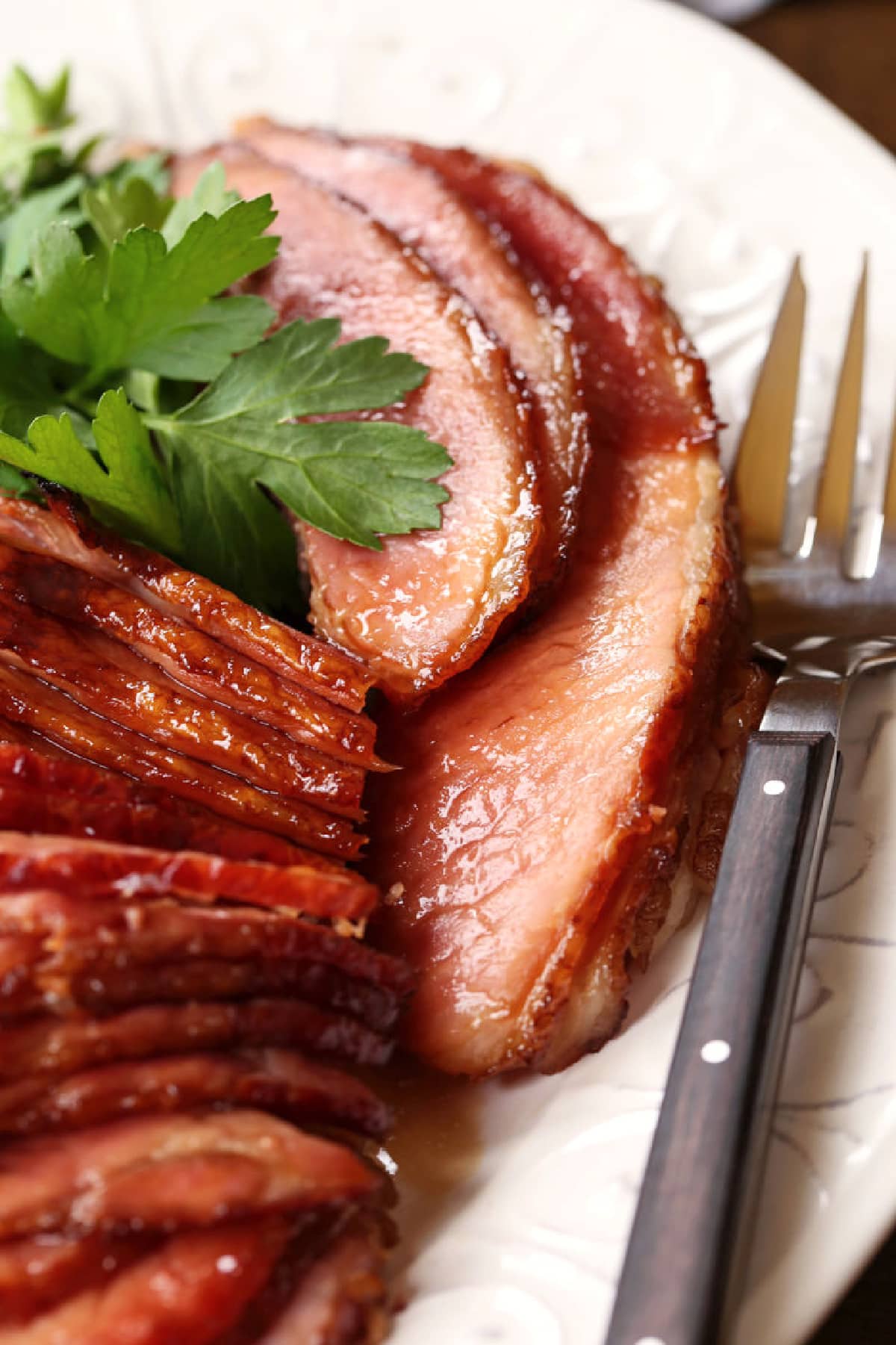 sliced spiral ham on a white platter with serving fork and parsley