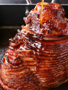 spiral sliced ham in roasting pan with glaze being poured over
