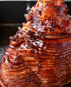 spiral sliced ham in roasting pan with glaze being poured over