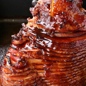 spiral sliced ham in roasting pan with glaze being poured over