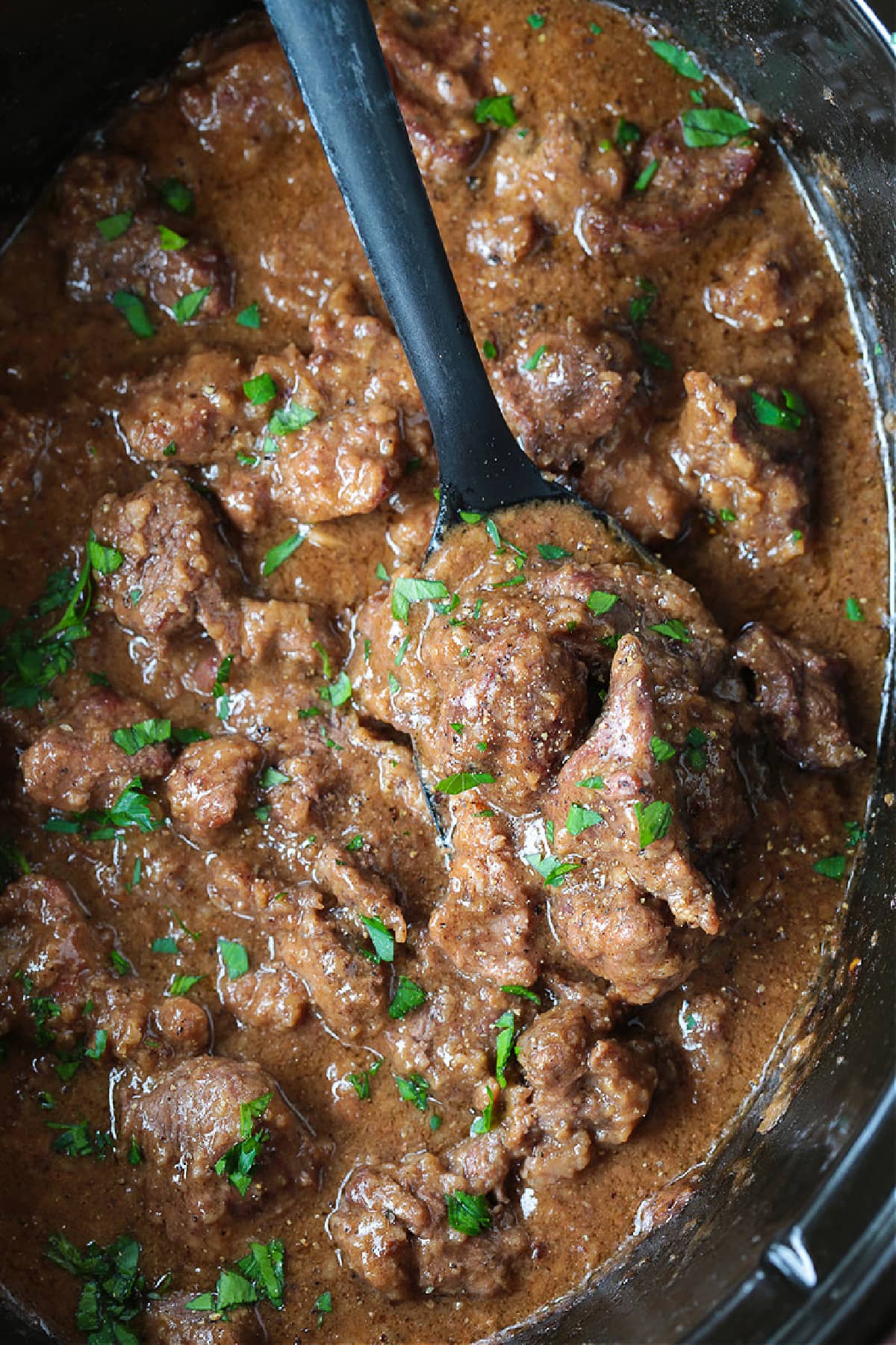 These Slow Cooker Beef Tips are a family favorite comfort food dinner. Spoon over mashed potatoes with lots of delicious brown gravy! beef tips and gravy in slow cooker with spoon