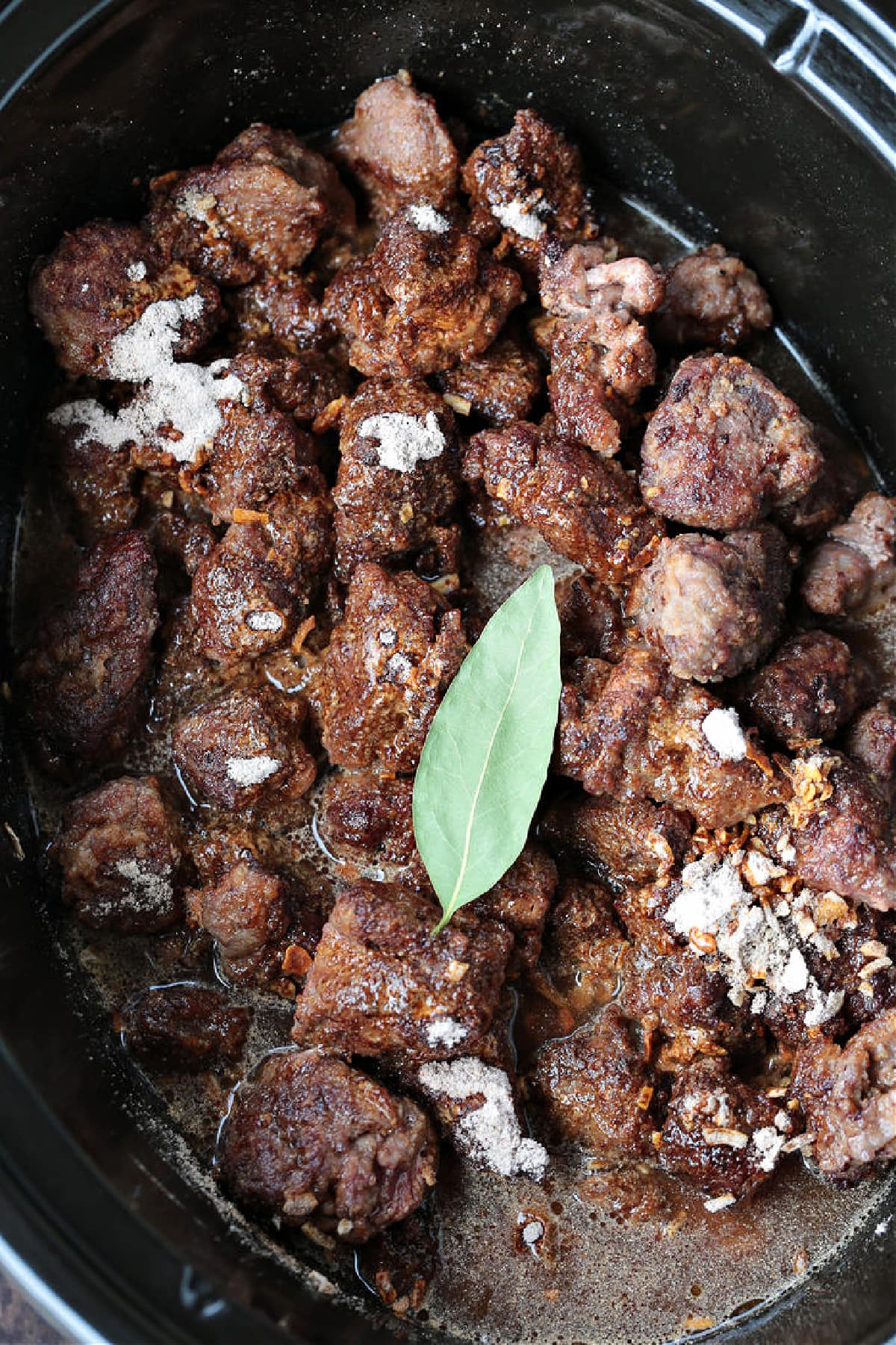 beef tips and bay leaf with seasonings in slow cooker
