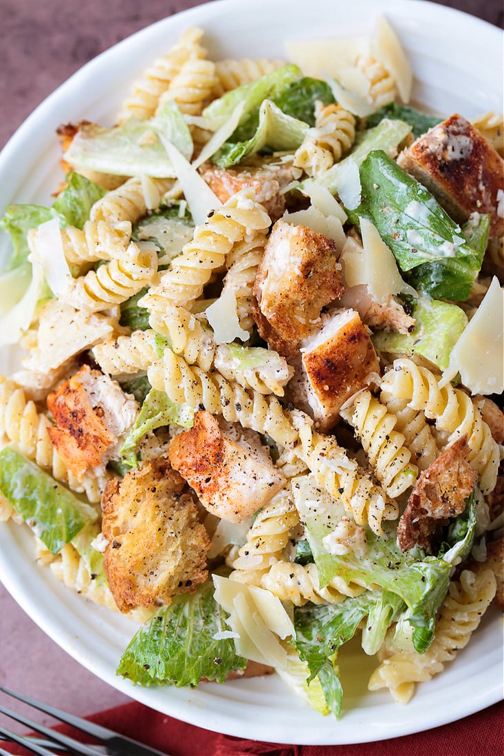 This Chicken Caesar Pasta Salad is bursting with flavor! Pasta tossed with lettuce and crunchy croutons, and our homemade Caesar dressing! pasta salad with lettuce and chicken on a white plate