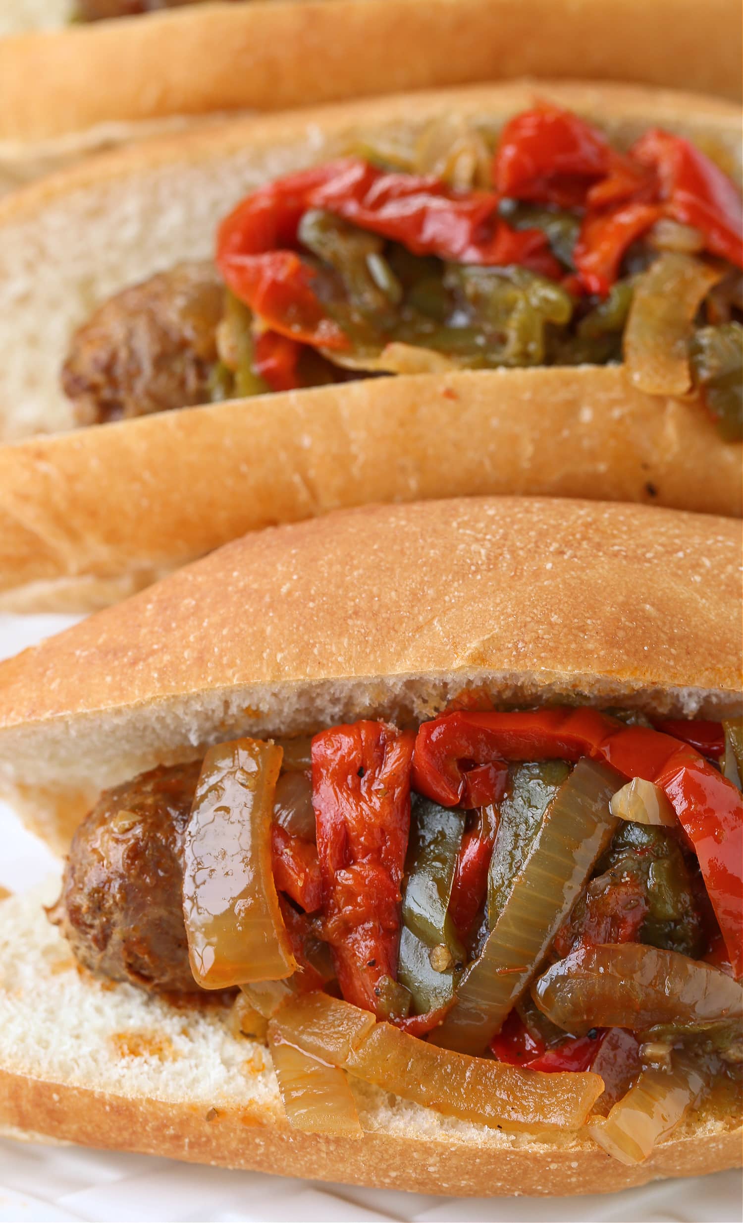 Our Crock Pot Sausage and Peppers are simmered in a marsala wine-tomato sauce that's so addicting! A fun dinner for parties and game days! sausage and pepper sandwiches close up on platter