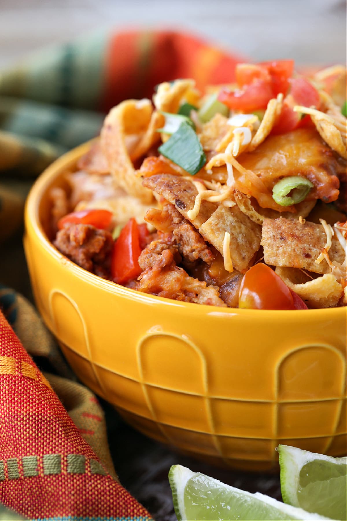 Kids and adults love this Frito Pie Recipe! A ground beef and bean casserole topped with crunchy Fritos corn chips and tons of cheese! frito pie in yellow bowl with napkin