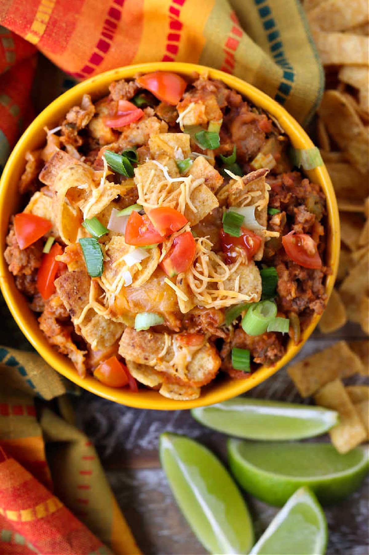 Kids and adults love this Frito Pie Recipe! A ground beef and bean casserole topped with crunchy Fritos corn chips and tons of cheese! Frito Pie casserole in a bowl with limes and chips on the side