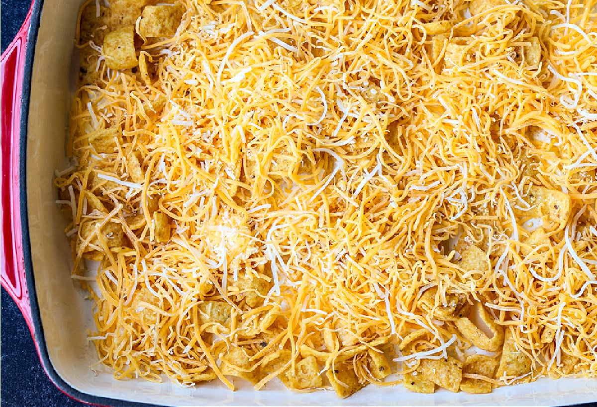 Kids and adults love this Frito Pie Recipe! A ground beef and bean casserole topped with crunchy Fritos corn chips and tons of cheese! shredded cheese in a casserole dish with Fritos