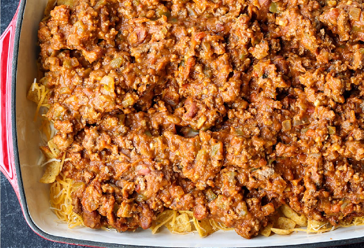 Kids and adults love this Frito Pie Recipe! A ground beef and bean casserole topped with crunchy Fritos corn chips and tons of cheese! ground beef with refried beans in casserole dish