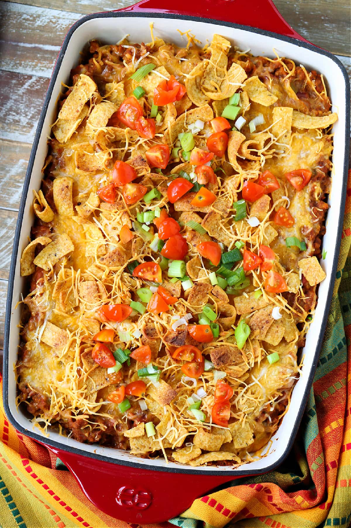 Kids and adults love this Frito Pie Recipe! A ground beef and bean casserole topped with crunchy Fritos corn chips and tons of cheese! Frito Pie casserole on a wood board with napkin