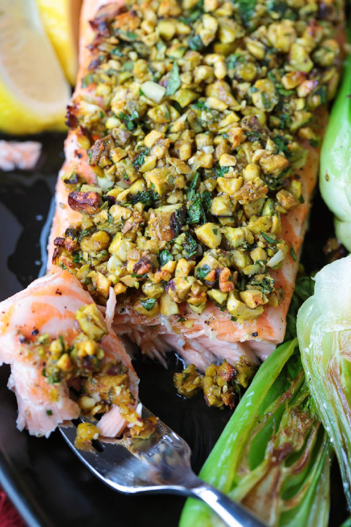 This Pistachio Crusted Salmon recipe is ready to serve in just 20 minutes! Perfectly cooked salmon with a pistachio, honey and garlic crust. fork with a bite of salmon on black platter