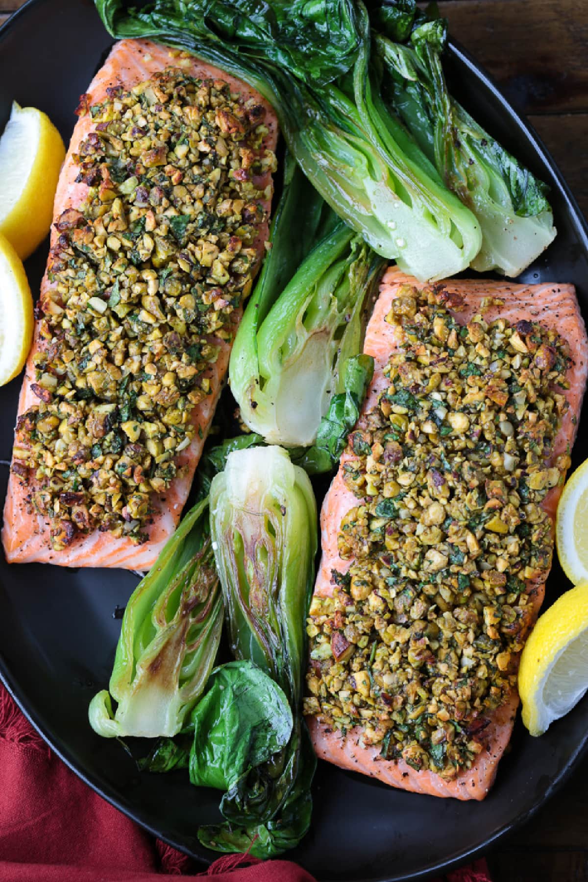 This Pistachio Crusted Salmon recipe is ready to serve in just 20 minutes! Perfectly cooked salmon with a pistachio, honey and garlic crust. black platter with pistachio crusted salmon and bok choy