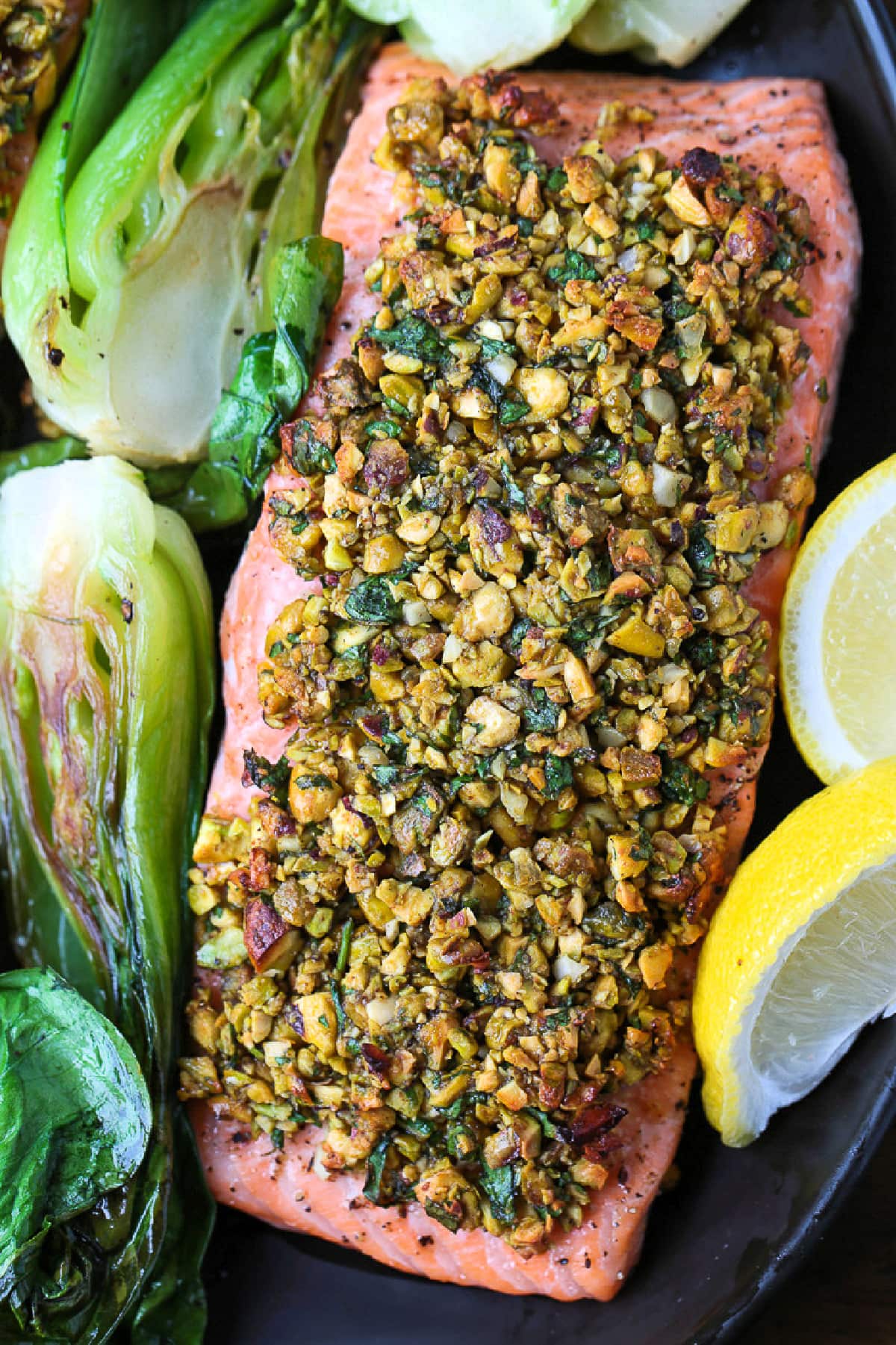 This Pistachio Crusted Salmon recipe is ready to serve in just 20 minutes! Perfectly cooked salmon with a pistachio, honey and garlic crust. black platter with pistachio crusted salmon and bok choy