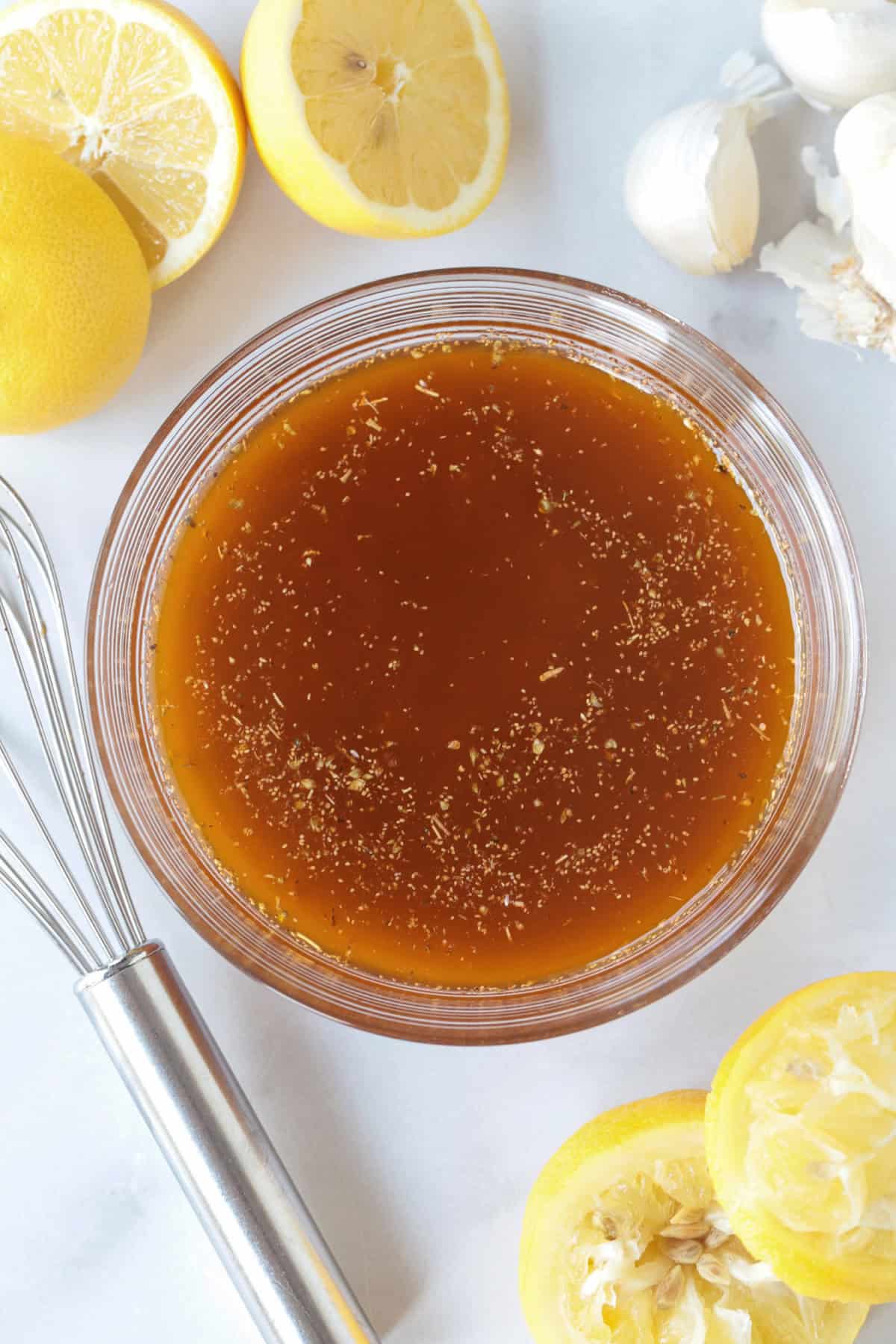 This Greek Chicken Marinade is super versatile! Lemon juice, garlic and oregano come together to make the most juicy, flavorful chicken. greek marinade in bowl with lemons and whisk