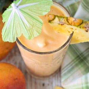 mango smoothie in glass with umbrella and fresh pineapple from top