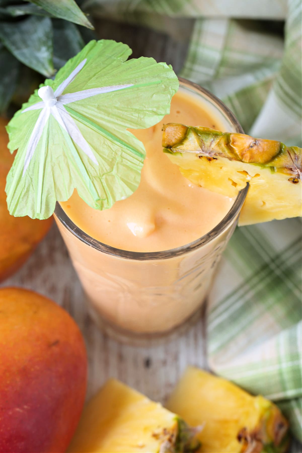 mango smoothie in glass with umbrella and fresh pineapple from top