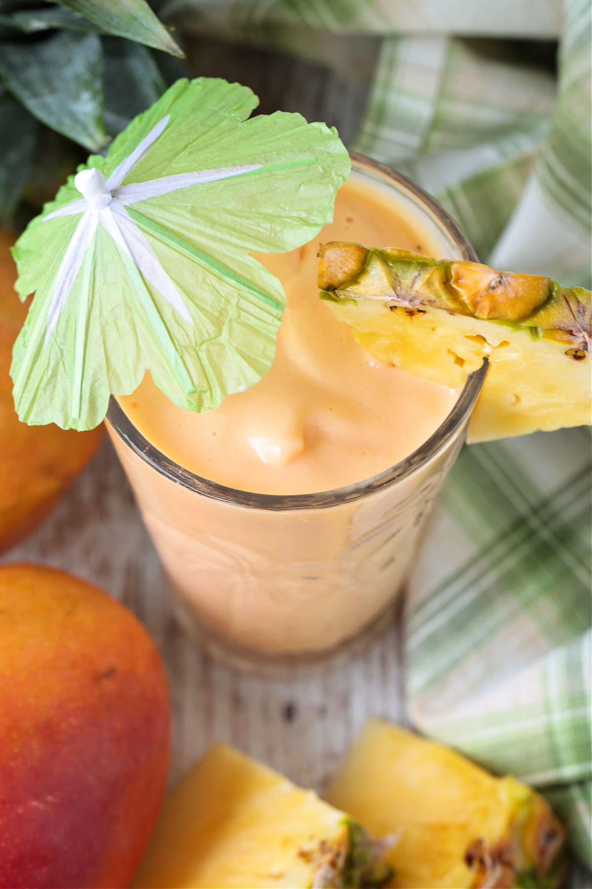 This Mango Pineapple Smoothie is so refreshing and tasty! Use fresh or frozen fruit to make this smoothie for breakfast, lunch or a snack! mango smoothie in glass with umbrella and fresh pineapple from top