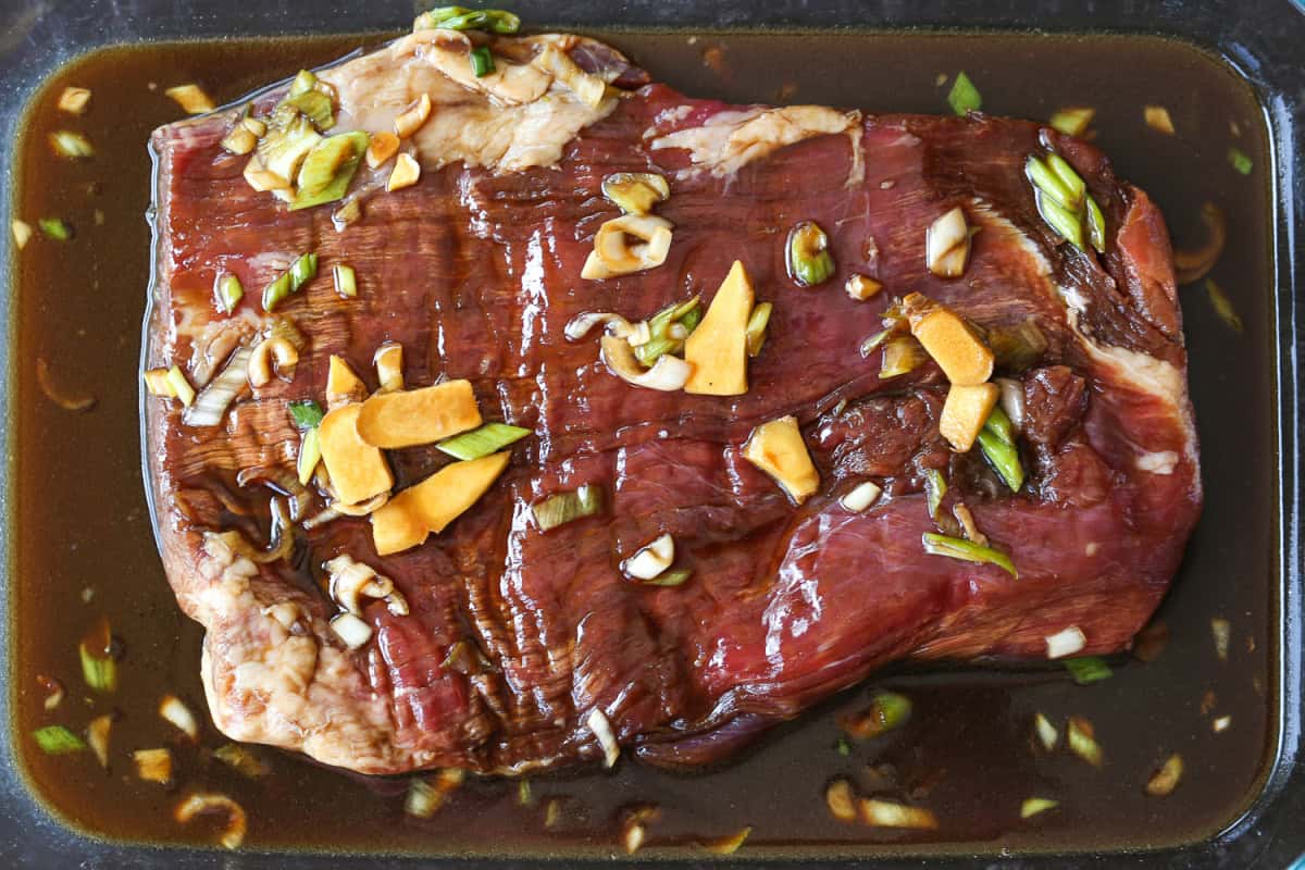 This addicting Teriyaki Steak recipe is super easy to make! A tasty, powerhouse marinade that adds flavor in just a short amount of time. flank steak marinating in glass dish