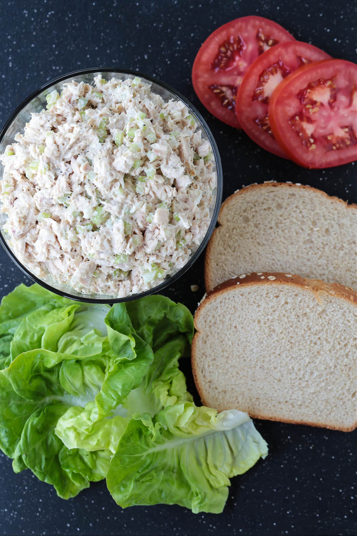 tuna fish salad with bread, tomatoes and lettuce on a board