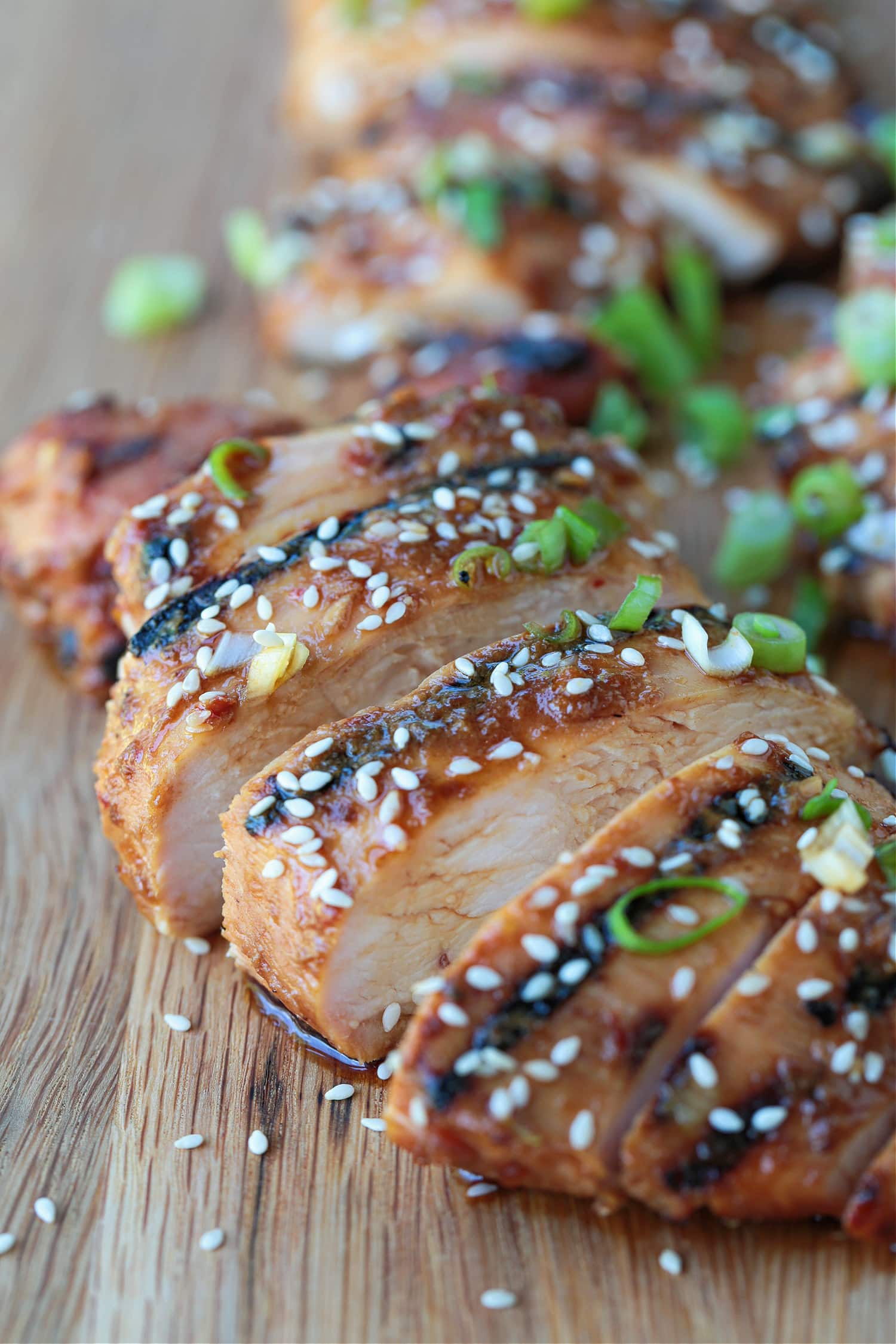 This Asian Chicken Marinade makes the most flavorful chicken! The bright flavors in this marinade will make any chicken delicious and juicy! sliced chicken on a board with sesame seeds and scallions