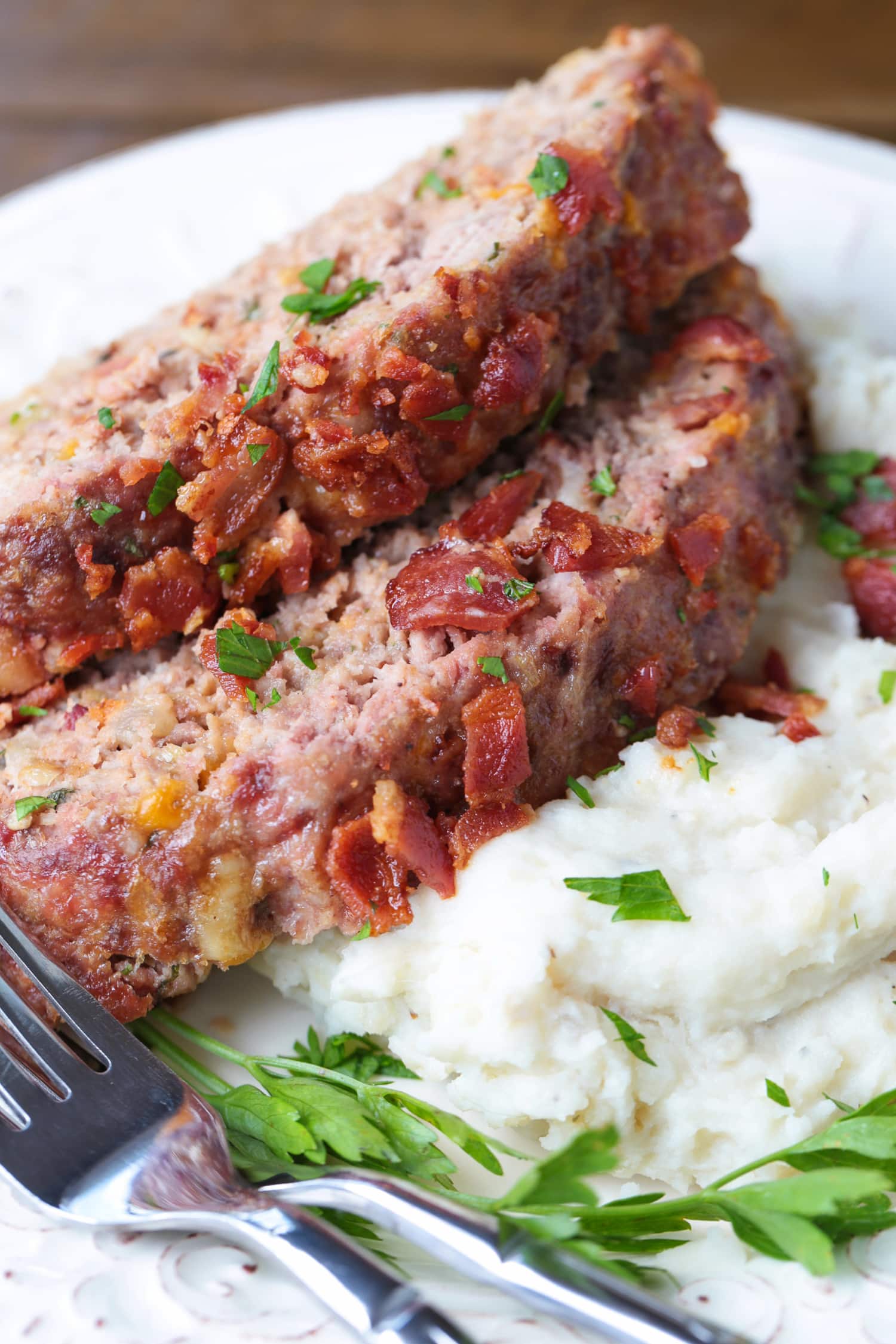 What could be more comforting than a Bacon Meatloaf for dinner? A delicious meatloaf recipe with cheddar cheese and lots of crispy bacon! sliced bacon meatloaf on a bed of mashed potatoes
