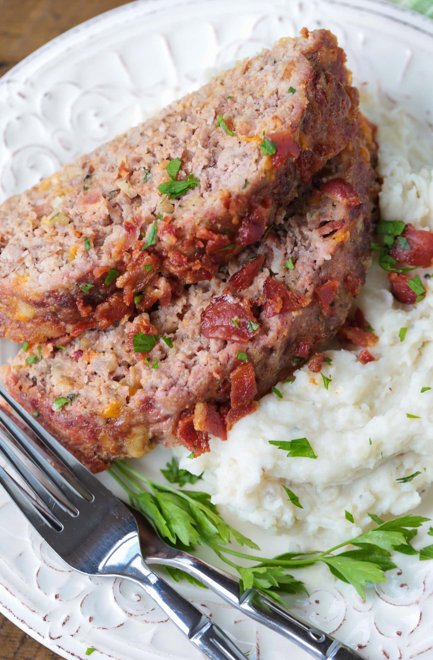 What could be more comforting than a Bacon Meatloaf for dinner? A delicious meatloaf recipe with cheddar cheese and lots of crispy bacon! sliced meatloaf with bacon and mashed potatoes