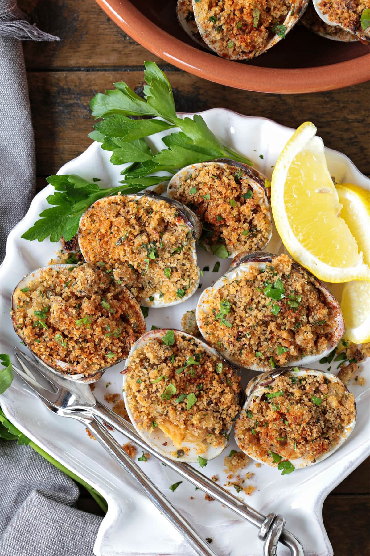 Baked Clams are always a hit! Fresh, steamed clams topped with a buttery breadcrumb topping. A delicious seafood appetizer or dinner! baked clams in shell dish with lemons and parsley