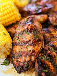 grilled balsamic chicken breasts stacked on a platter with corn