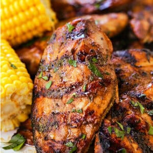 grilled balsamic chicken breasts stacked on a platter with corn