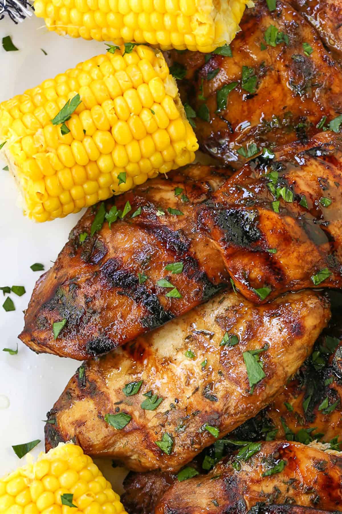Our Balsamic Chicken Marinade is delicious on any cut of chicken! Tangy and sweet with fresh, vibrant herbs that flavor chicken wonderfully. grilled chicken breasts on a platter with corn on the side