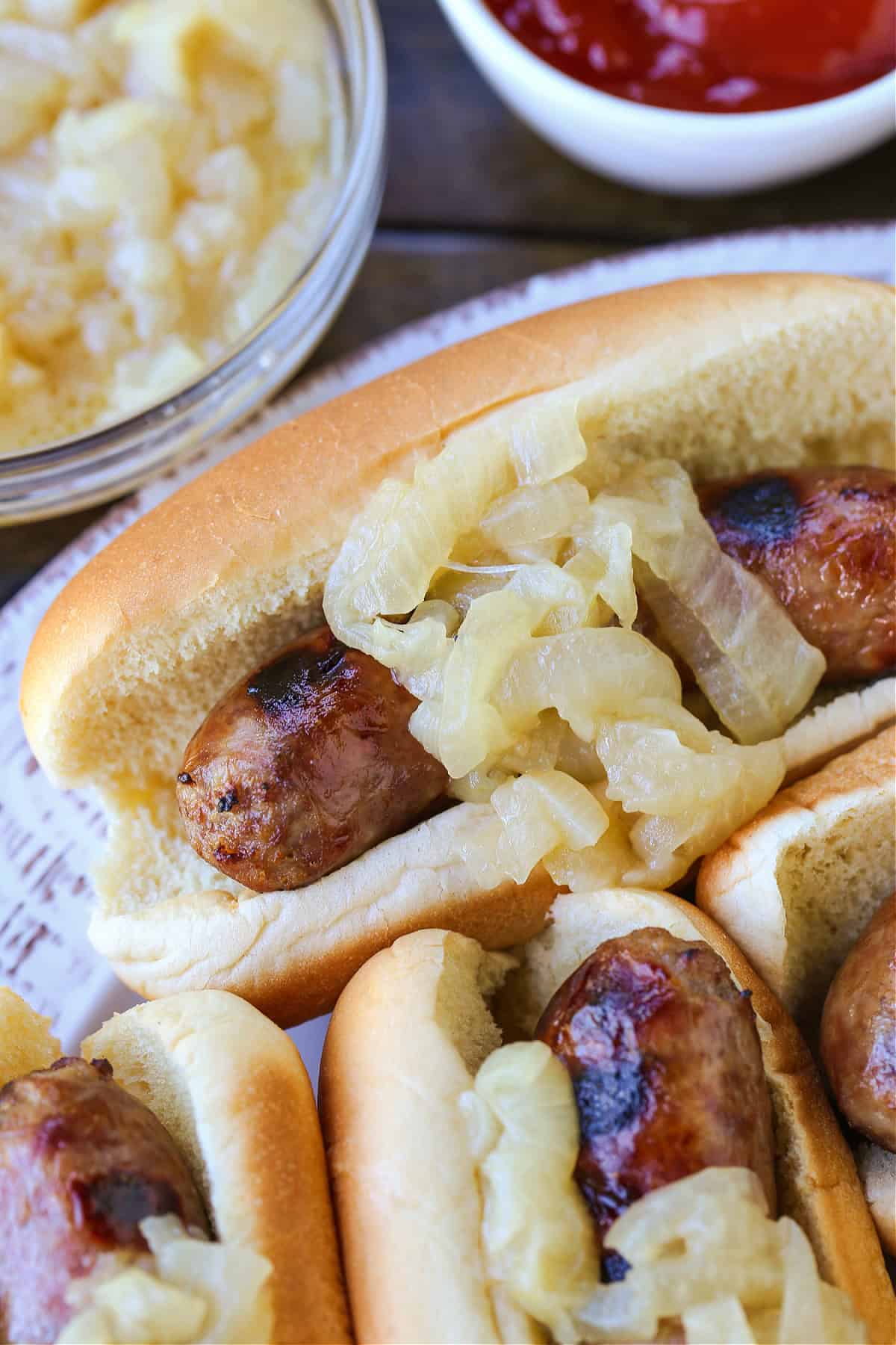 Beer Brats are a family favorite! Bratwurst cooked in beer, onions and our secret ingredient that makes them super tender and flavorful! bratwurst with onions on platter with ketchup