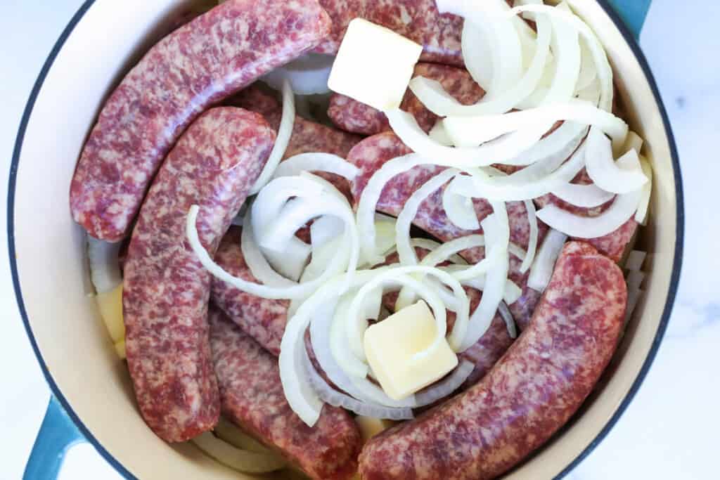 Beer Brats are a family favorite! Bratwurst cooked in beer, onions and our secret ingredient that makes them super tender and flavorful! raw bratwurst with onions and butter in pot