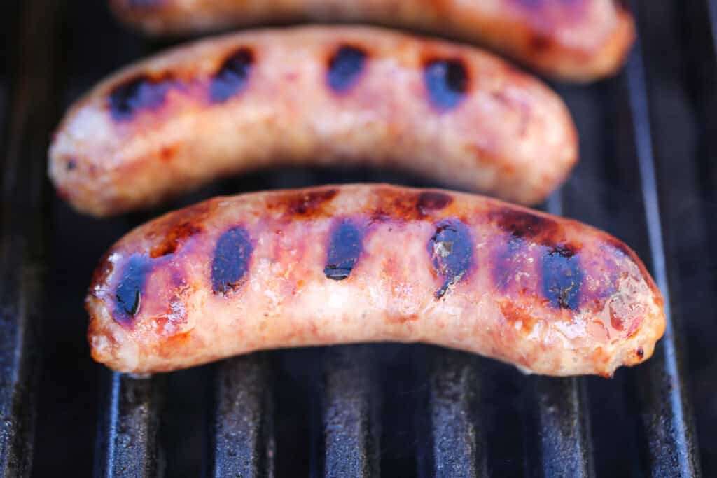 Beer Brats are a family favorite! Bratwurst cooked in beer, onions and our secret ingredient that makes them super tender and flavorful! bratwurst on grill with grill marks