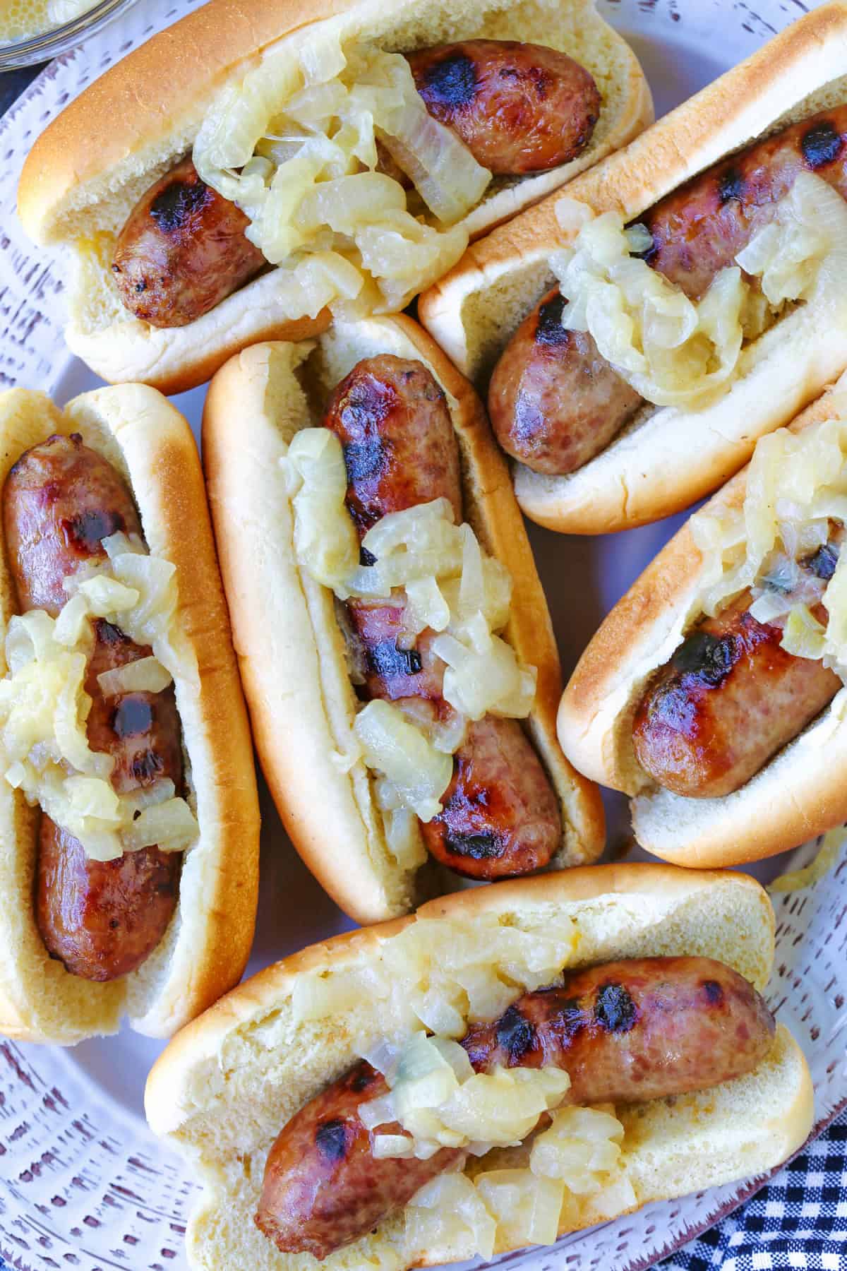 Beer Brats are a family favorite! Bratwurst cooked in beer, onions and our secret ingredient that makes them super tender and flavorful! bratwurst with onions on buns on platter