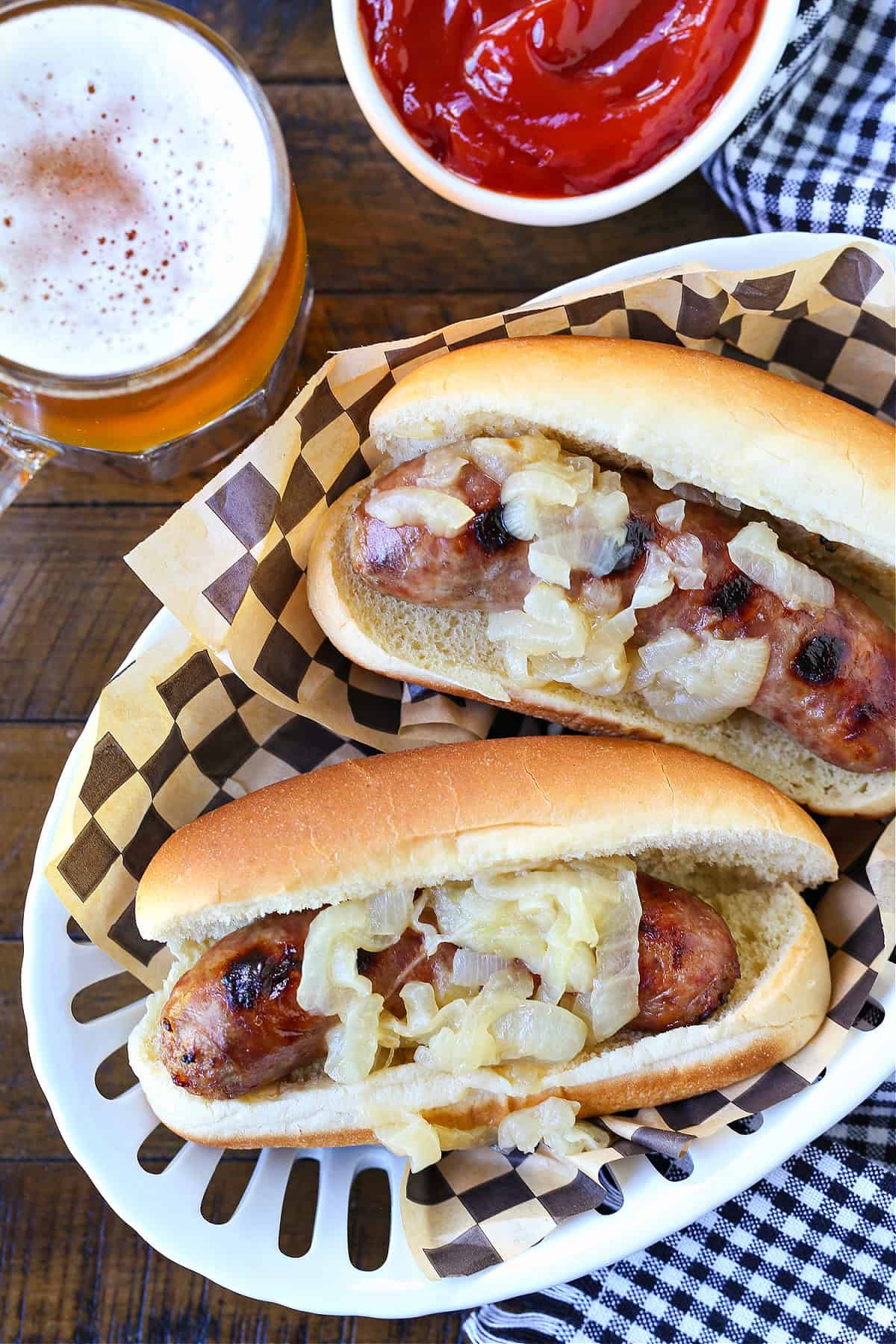 Beer Brats are a family favorite! Bratwurst cooked in beer, onions and our secret ingredient that makes them super tender and flavorful! bratwurst with onions in basket with beer and ketchup