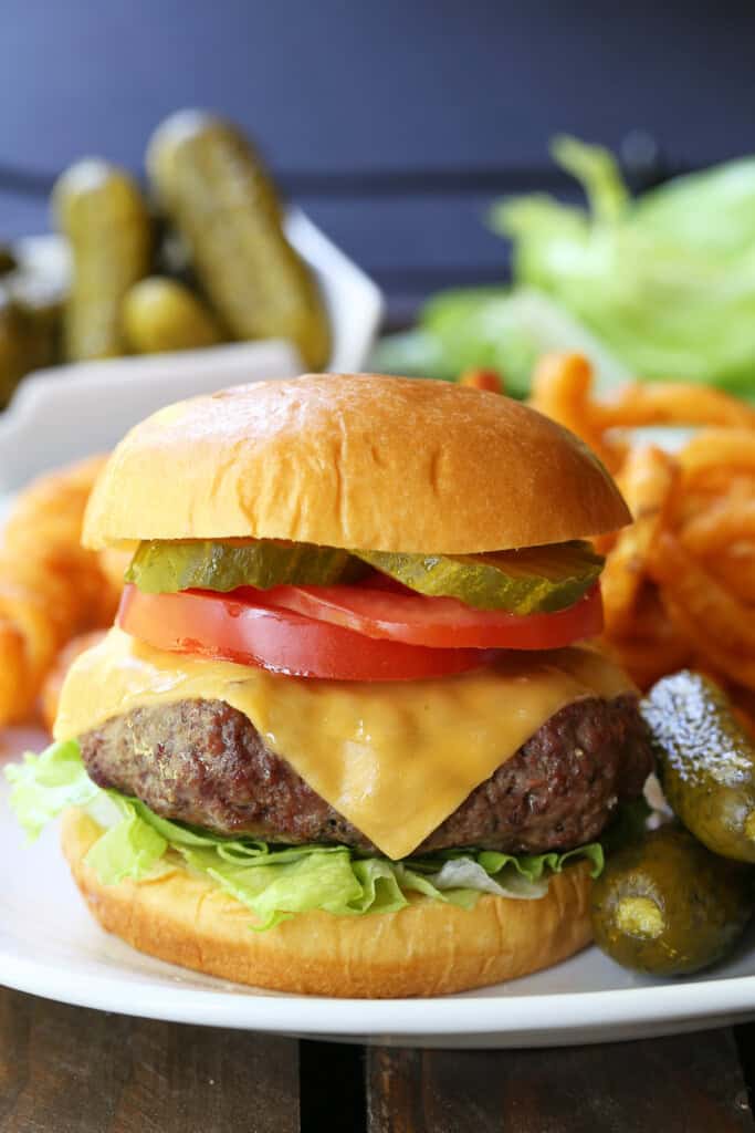 cheeseburger with toppings on plate with pickles and fries