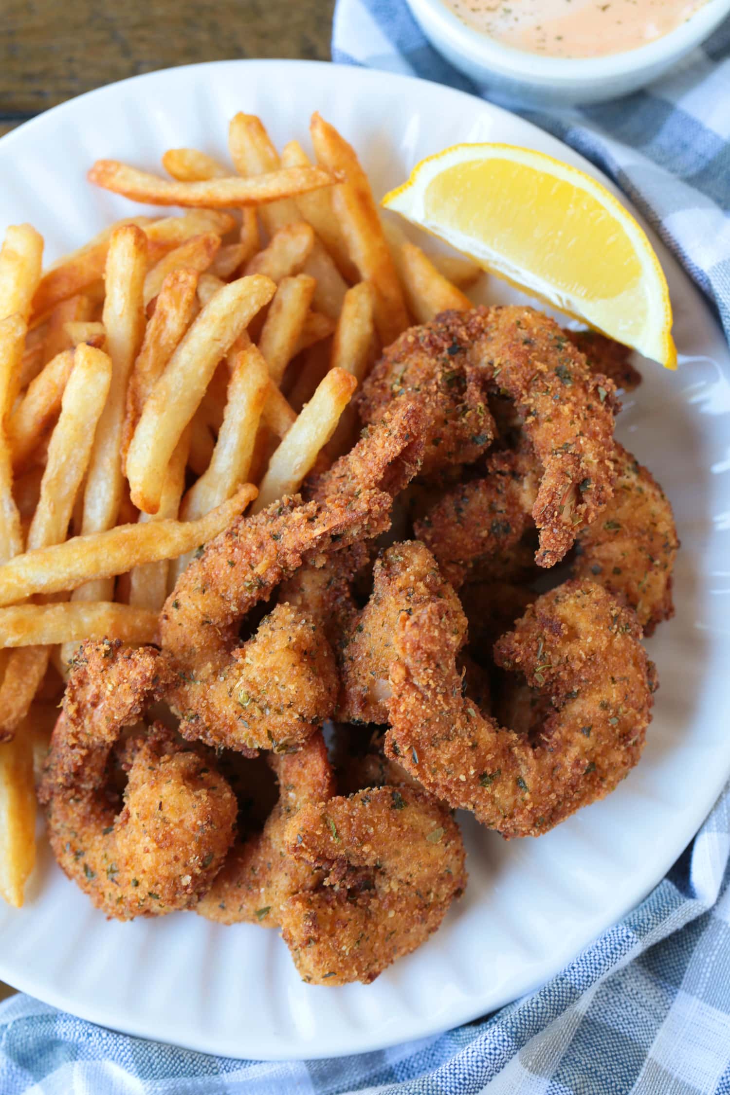 breaded shrimp on a plate with fries and lemon wedge
