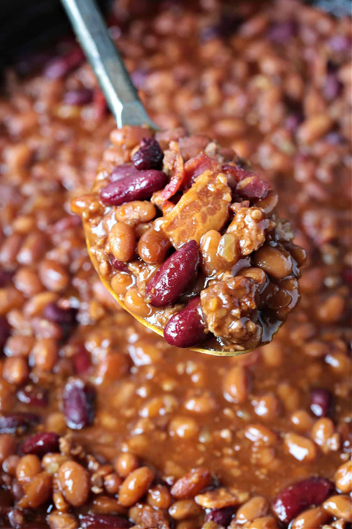 baked beans with ground beef and bacon on serving spoon