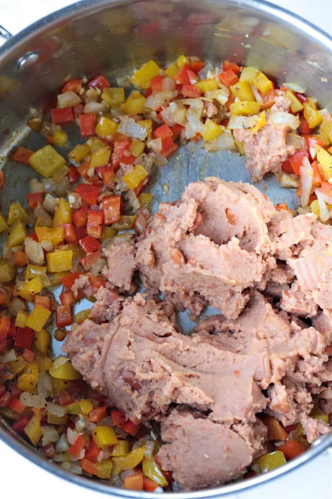 Our Chicken Fajita Soup is packed with protein! A secret ingredient makes this soup thick and creamy, without any cream or cream cheese! refried beans in a pot with peppers and onions