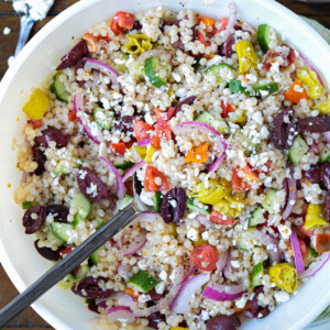 greek couscous salad in bowl with feta and dressing on side