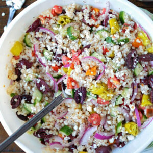 greek couscous salad in bowl with feta and dressing on side