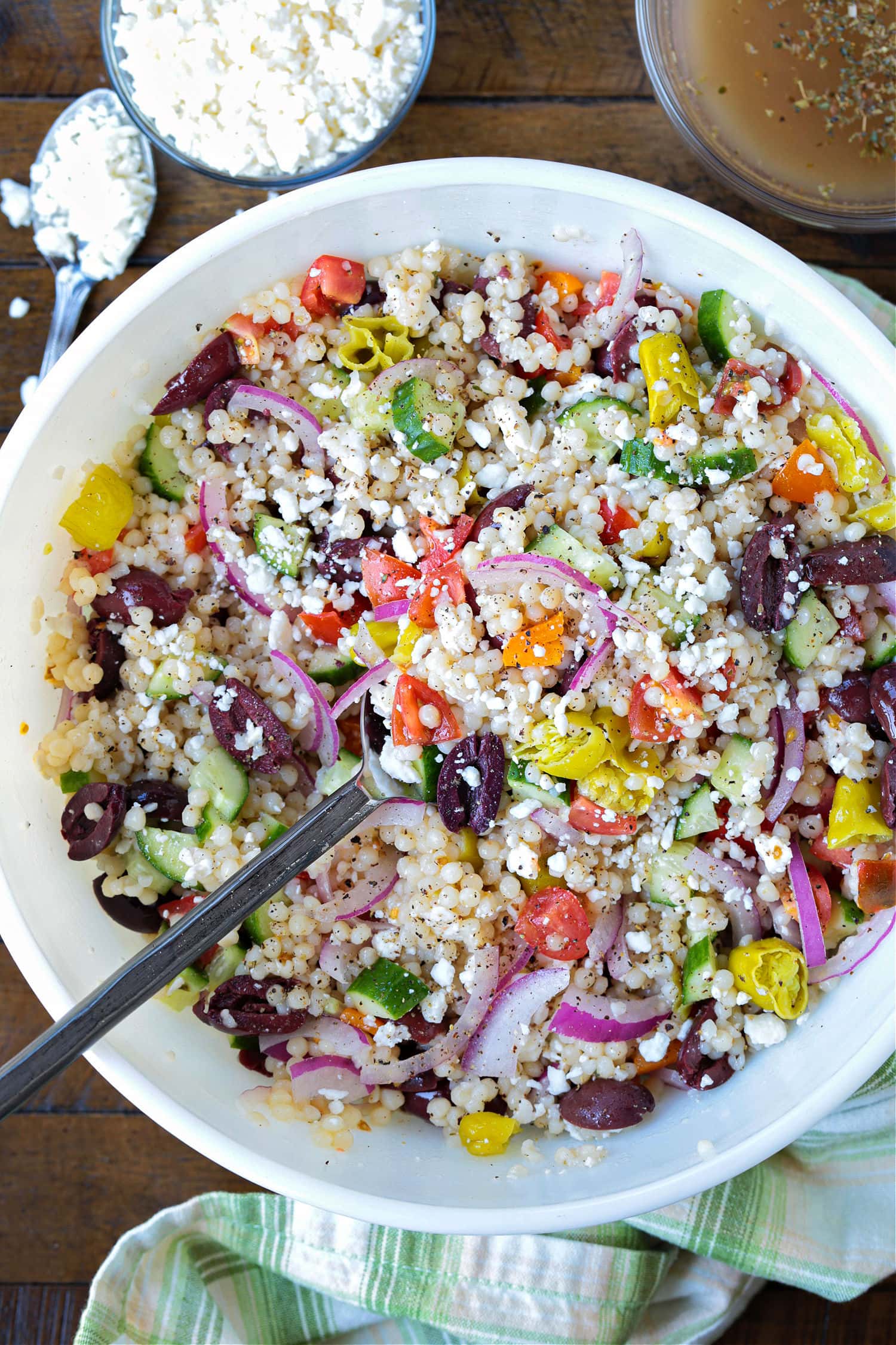 greek couscous salad in bowl with feta and dressing on side