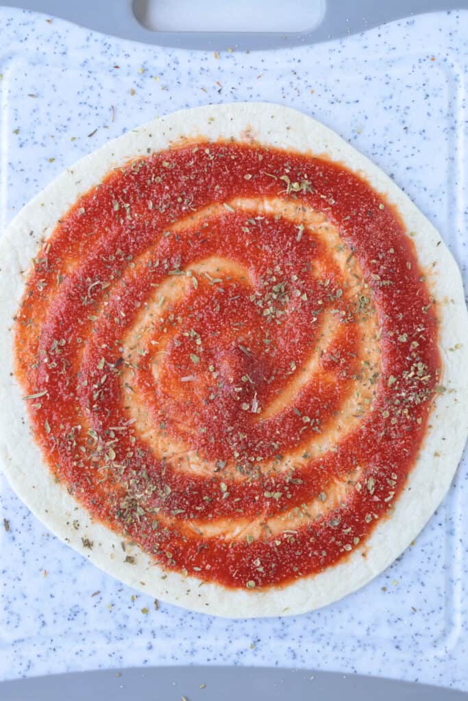 An Air Fryer Tortilla Pizza is perfect for an after school snack or an easy meal! A thin, crispy crust with gooey cheese ready in minutes! tomato sauce on tortilla seasoned with oregano