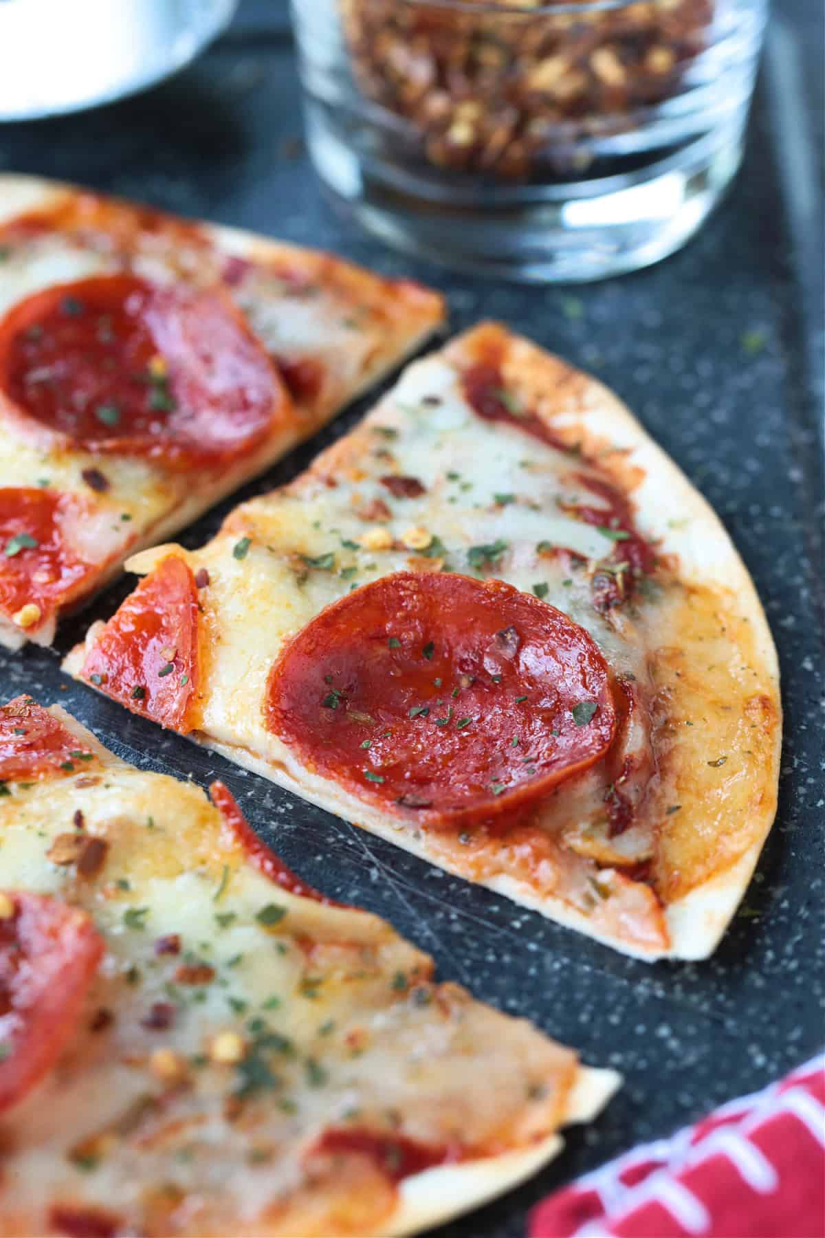 An Air Fryer Tortilla Pizza is perfect for an after school snack or an easy meal! A thin, crispy crust with gooey cheese ready in minutes! tortilla pizza cut into a wedge
