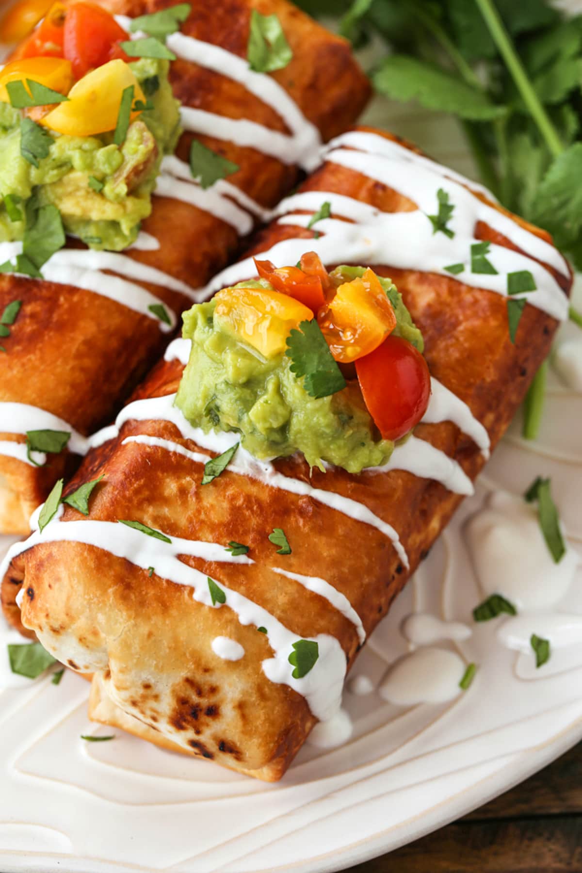 Chicken Chimichangas are super crispy and oozing with flavor! A chicken and cheese filling tucked inside a crispy, pan-fried tortilla. Chicken Chimichangas on a plate with sour cream drizzle