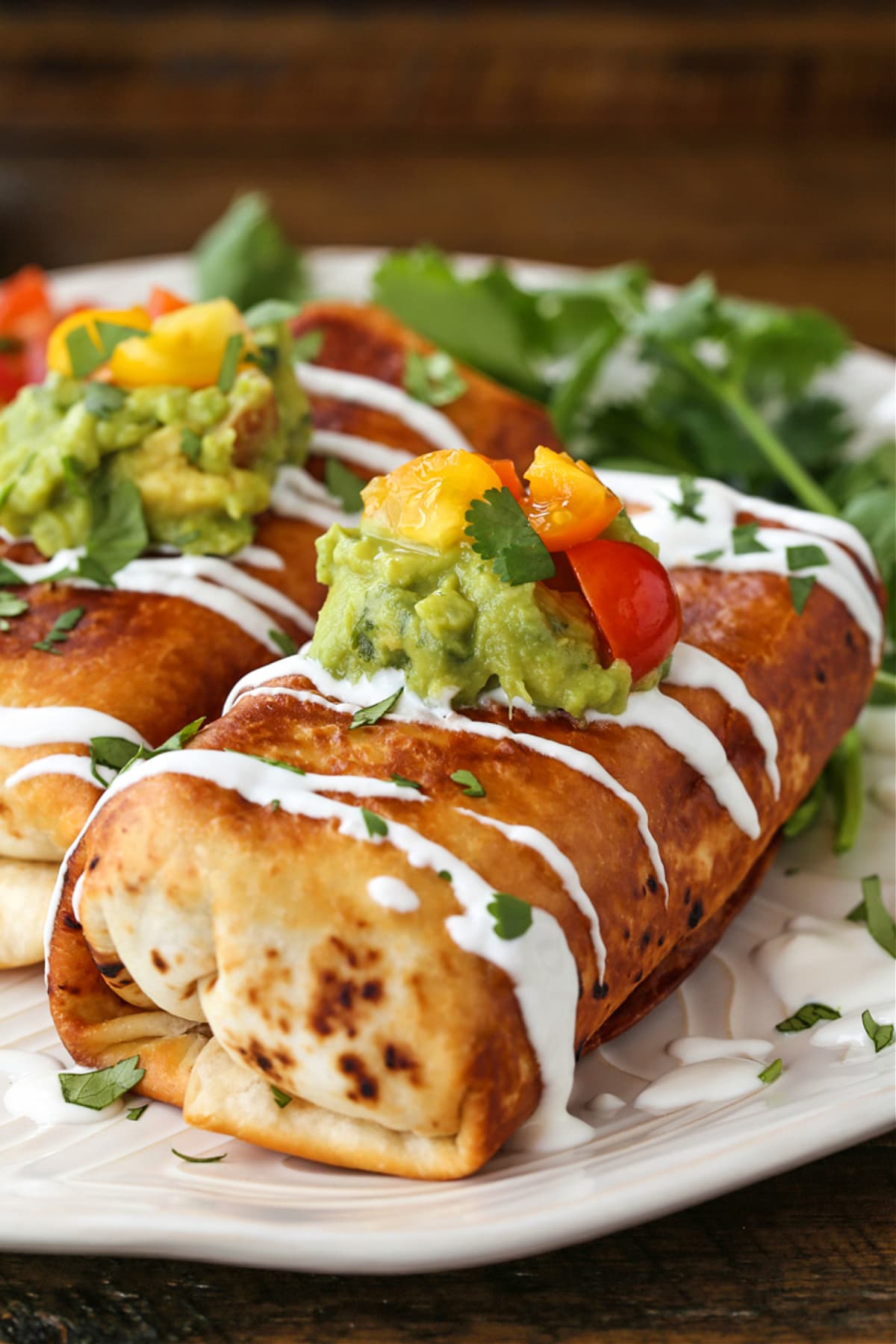 Chicken Chimichangas are super crispy and oozing with flavor! A chicken and cheese filling tucked inside a crispy, pan-fried tortilla. chicken chimichangas on a plate with toppings and sour cream drizzle