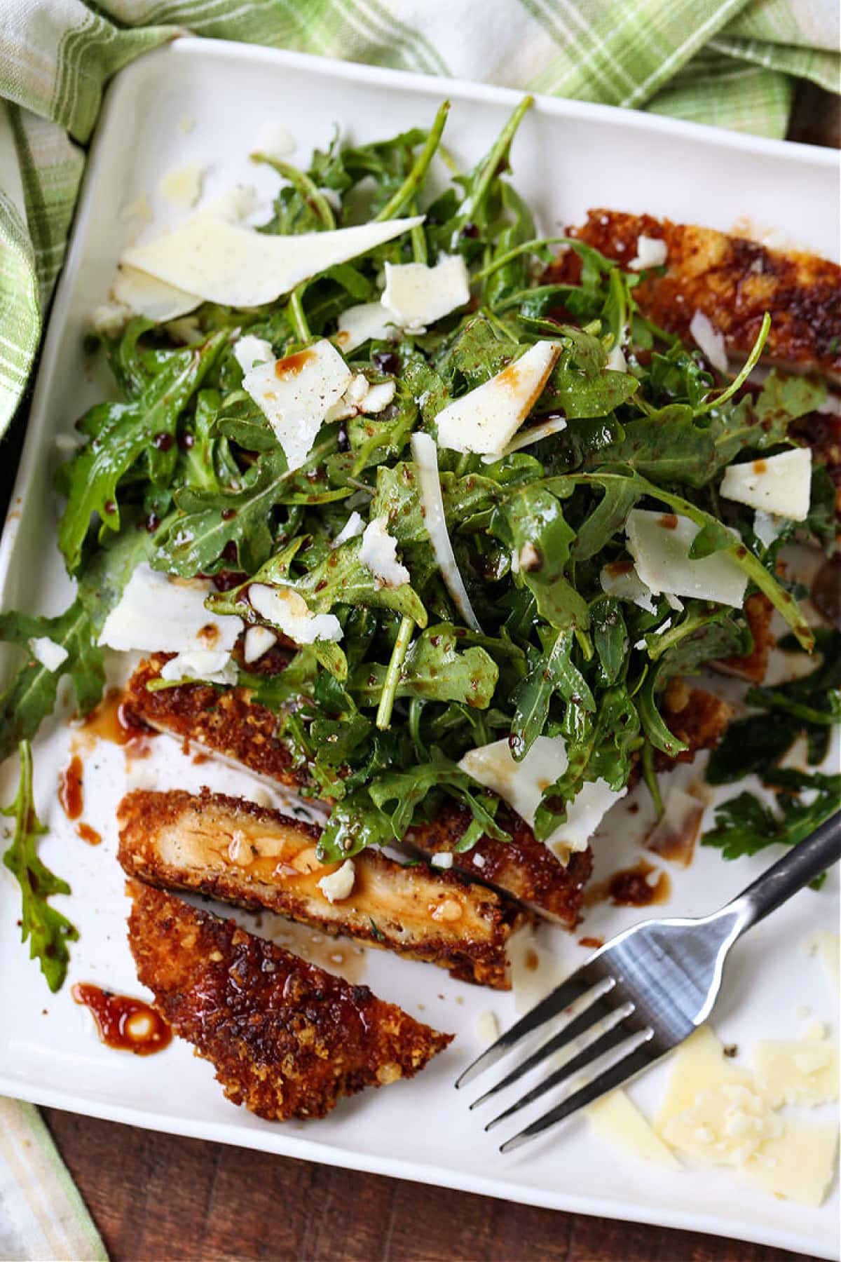 Chicken Milanese is an easy, restaurant quality dish that's ready in just 30 minutes! Warm chicken cutlets topped with a crisp arugula salad! Chicken Milanese on a white plate with fork